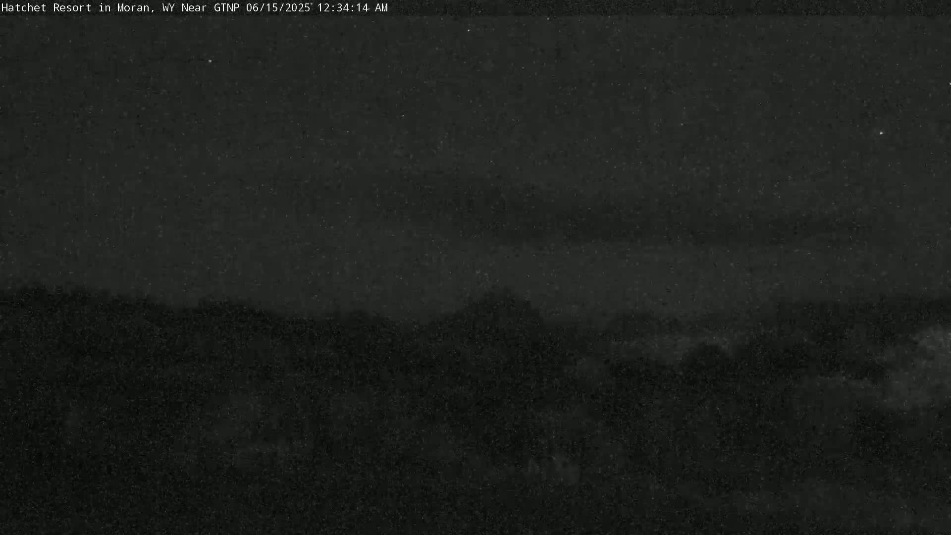 A nighttime, low-light view shows a dark landscape with a mountainous horizon under a mostly clear, starry sky.