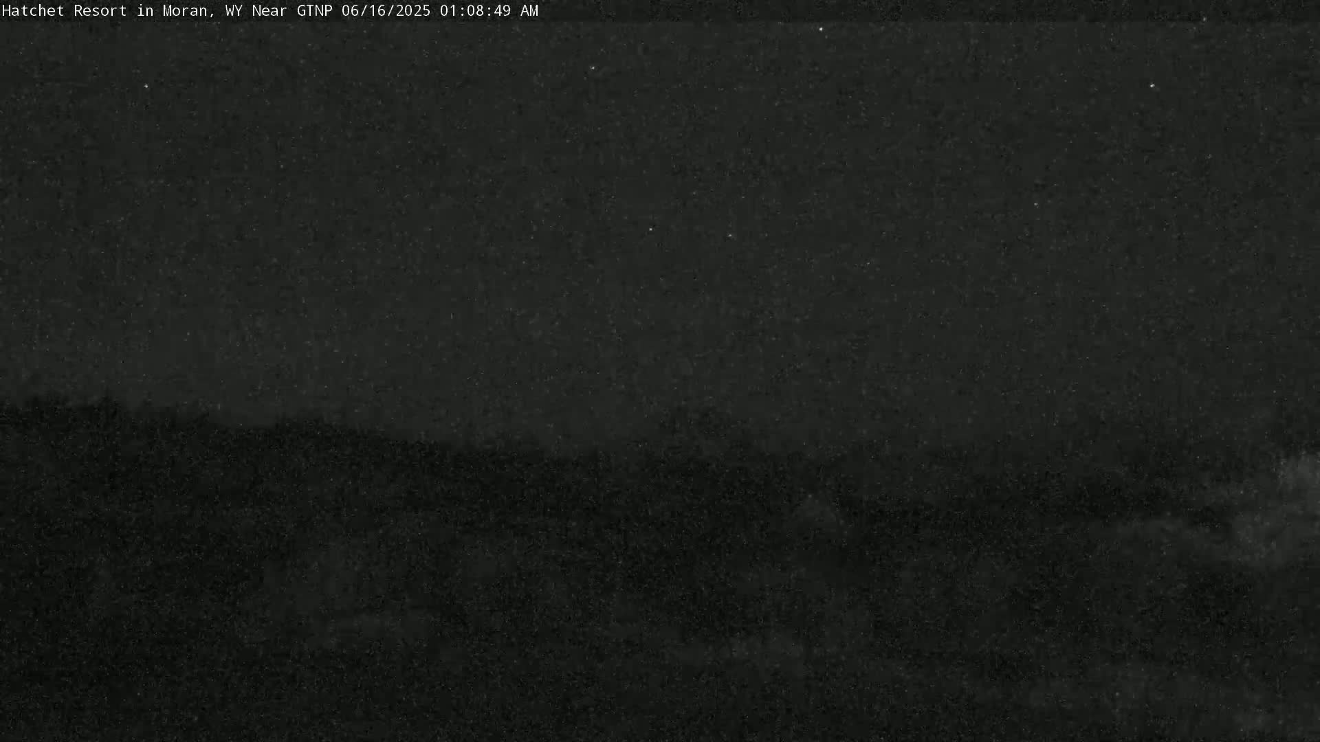 A nighttime, low-light view of a dark landscape under a mostly clear, starry sky.
