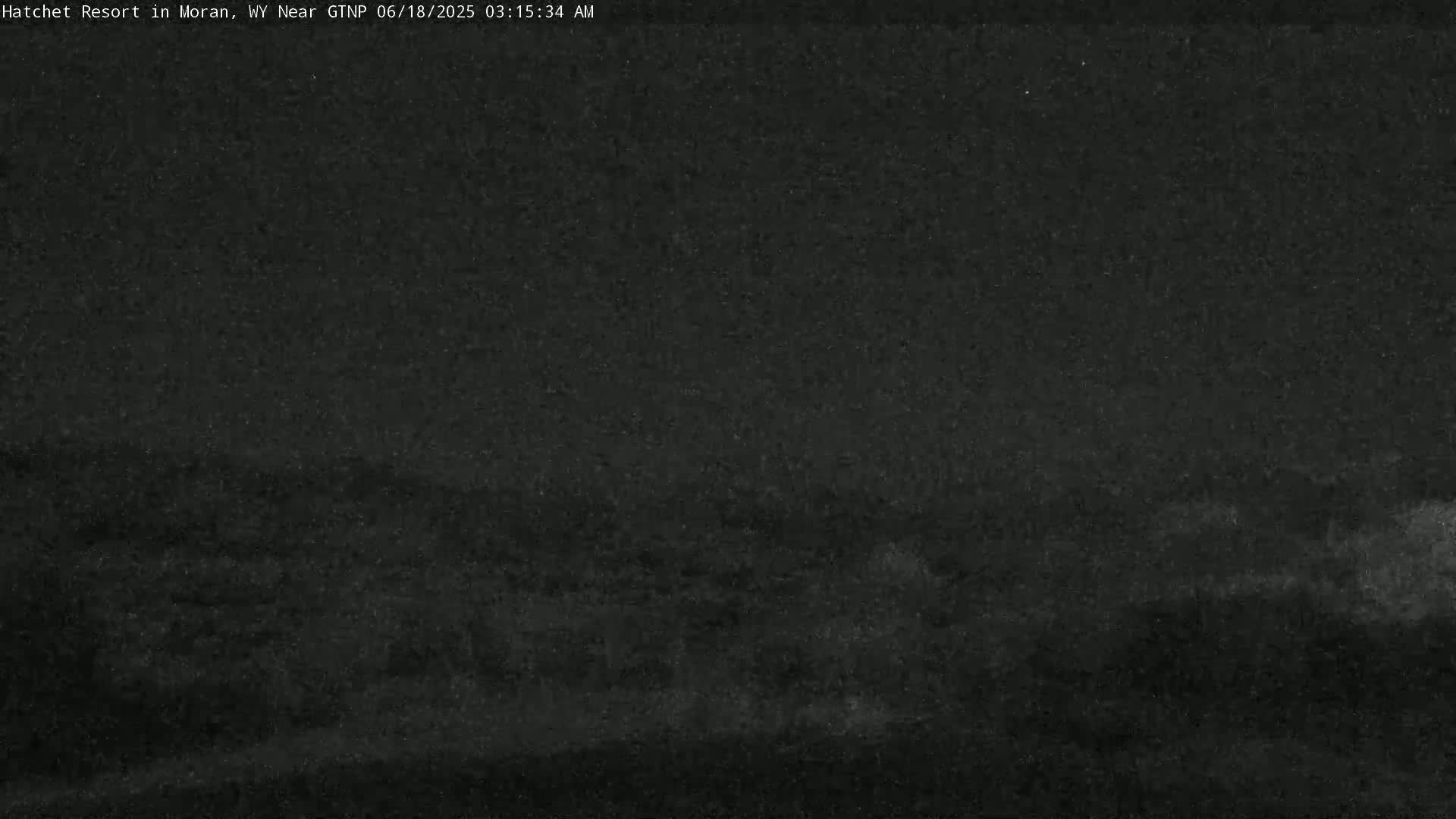 A low-light, nighttime outdoor image shows a dark landscape under a mostly clear sky.