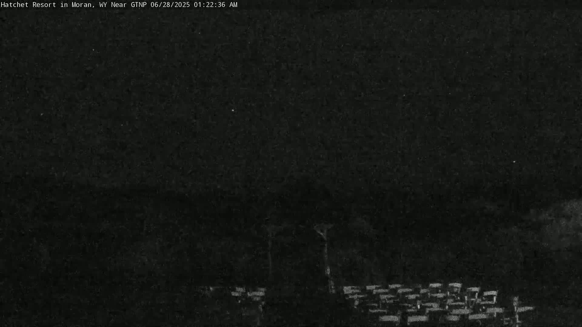 A low-light, nighttime image shows a dark, mostly obscured area with a few indistinct structures visible in the lower portion of the frame.