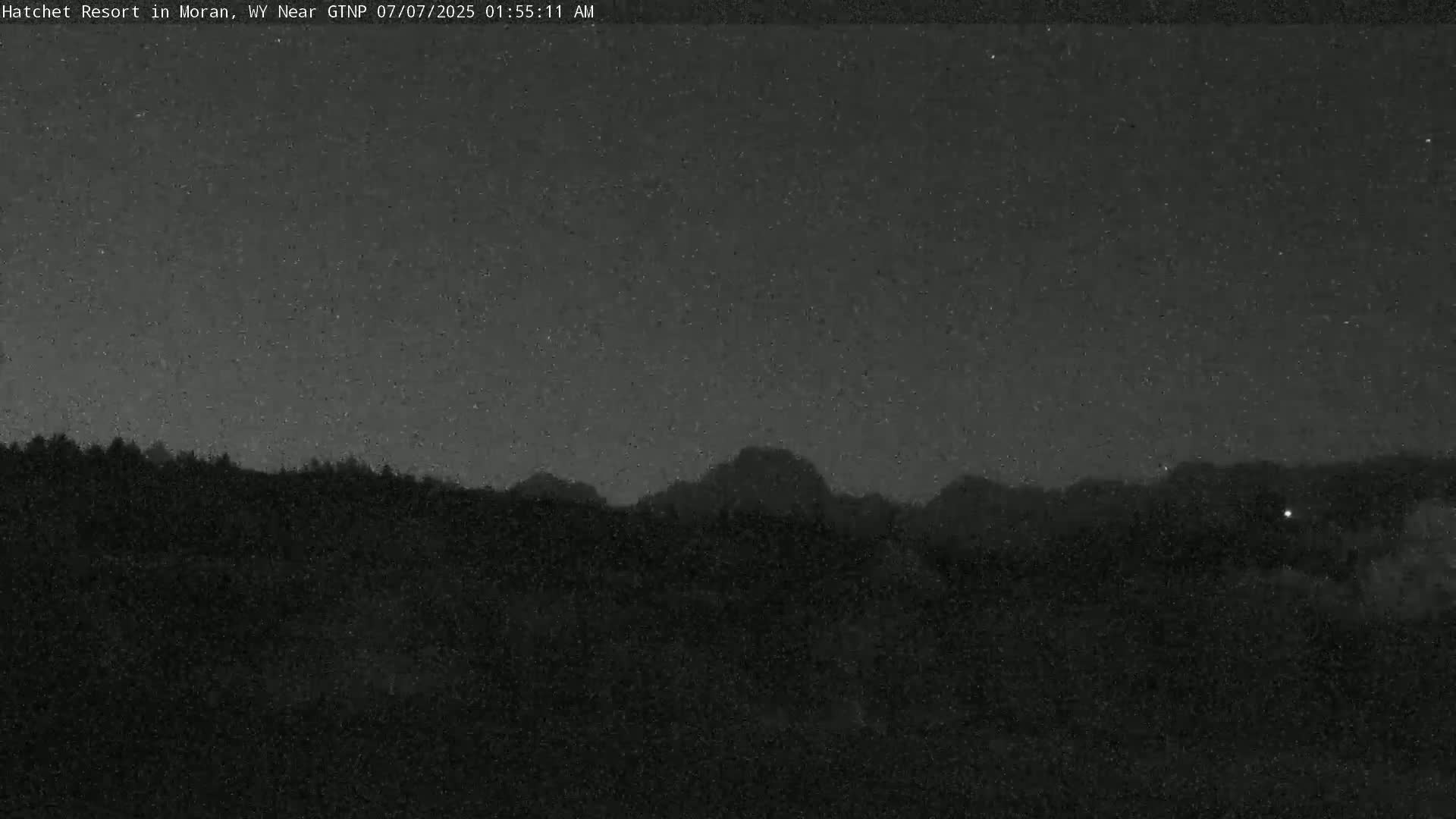 A nighttime view shows a dark, silhouetted mountain range under a mostly clear, star-speckled sky.