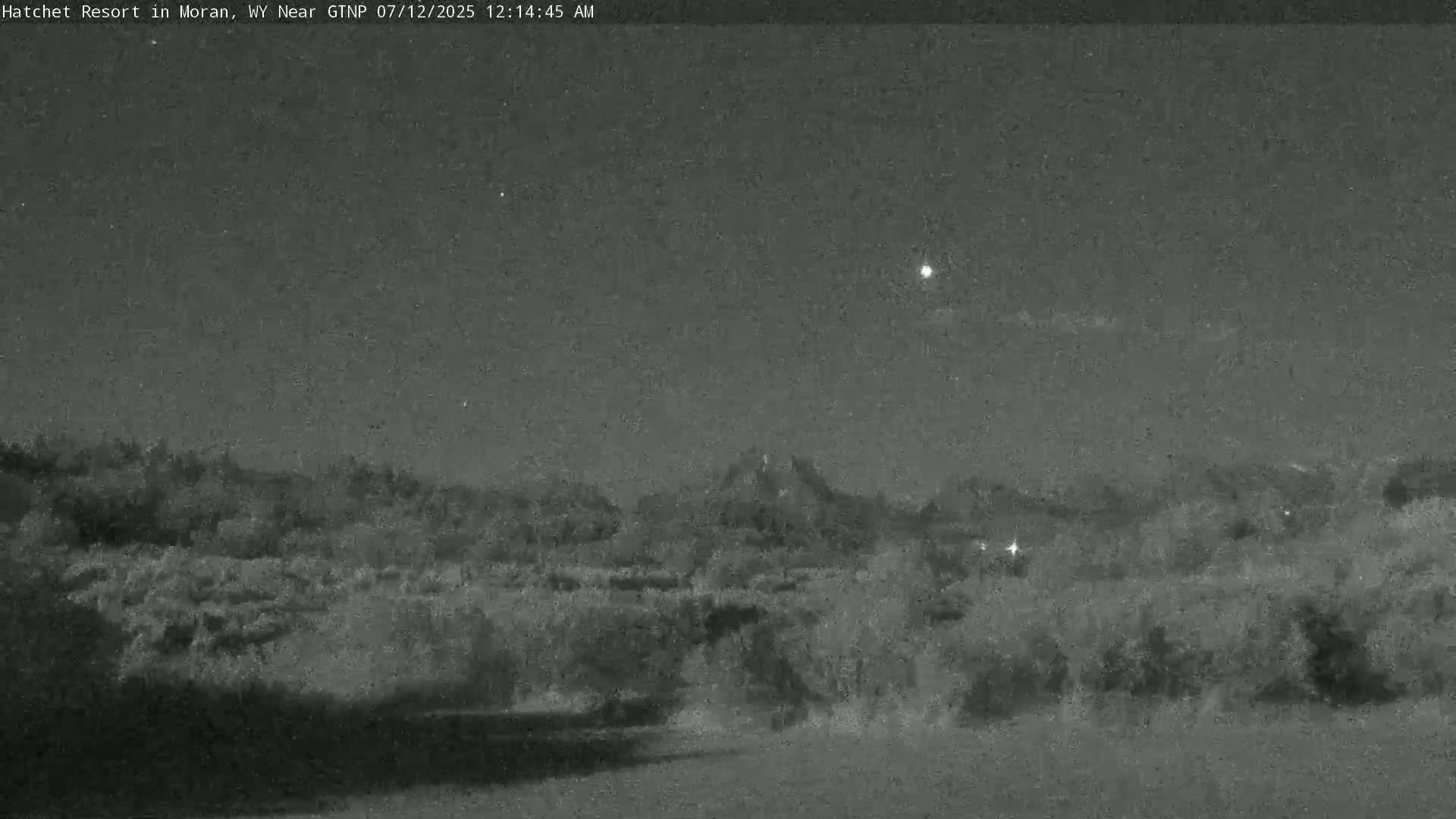 A nighttime view shows a dark, silhouetted mountain range under a mostly clear, star-speckled sky.
