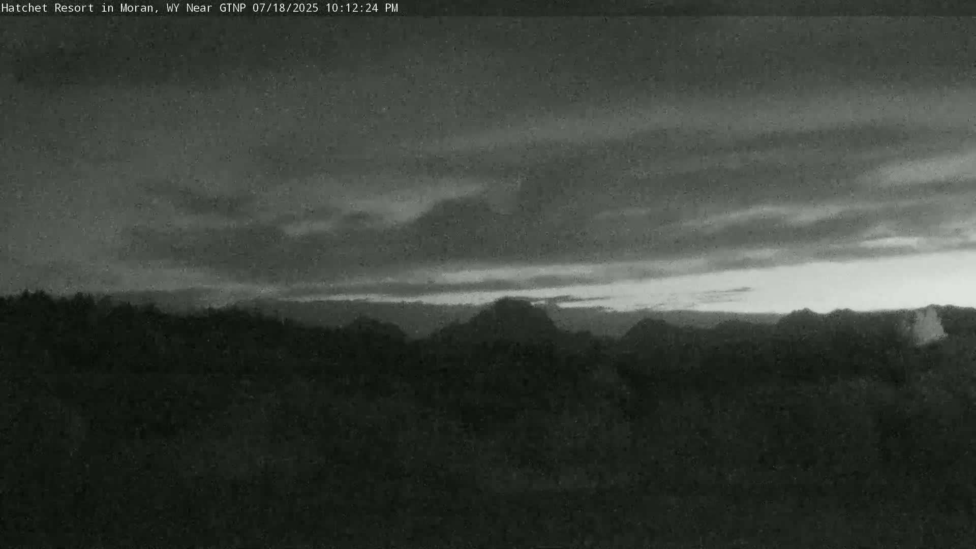 A grayscale image shows a dark, overcast sky over a line of distant, dark hills and trees.