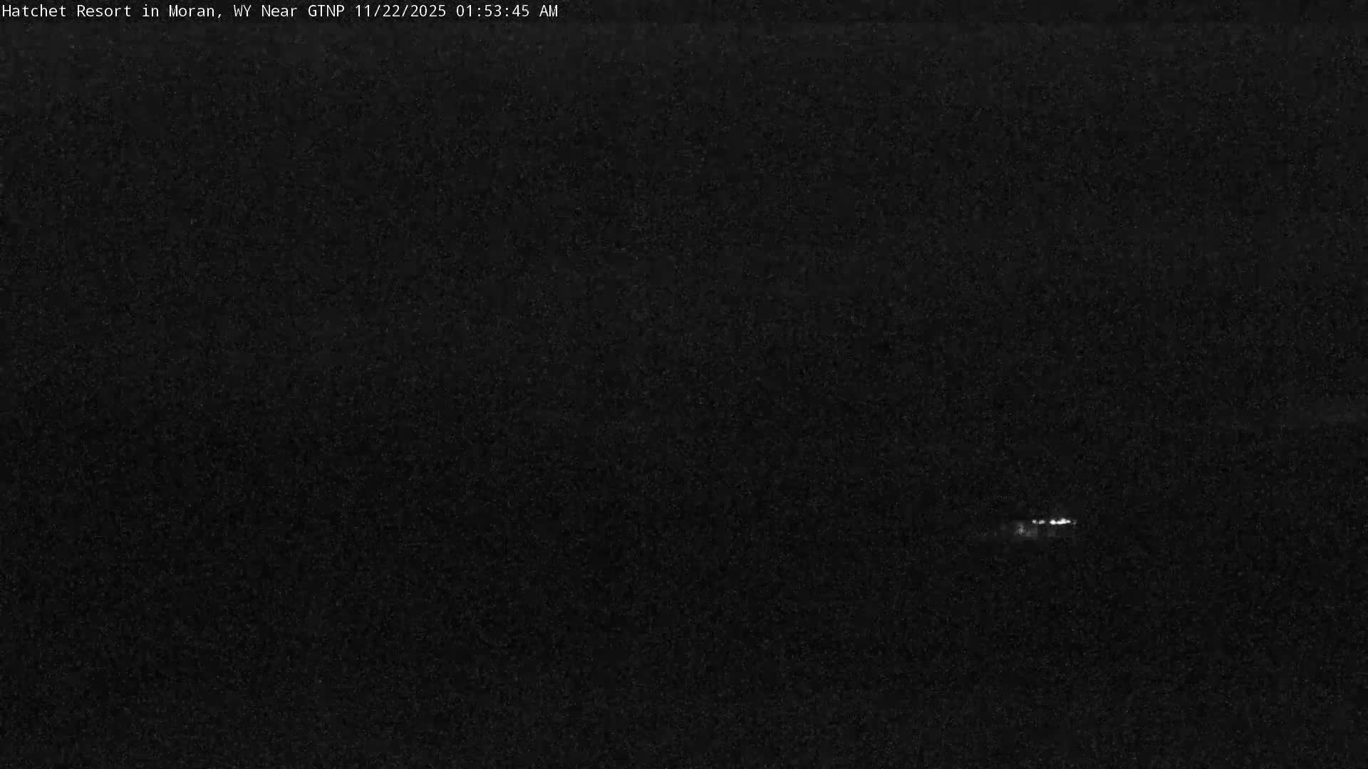 The image displays an extremely dark, grainy outdoor scene at night, revealing only a few faint, distant lights in the lower right.