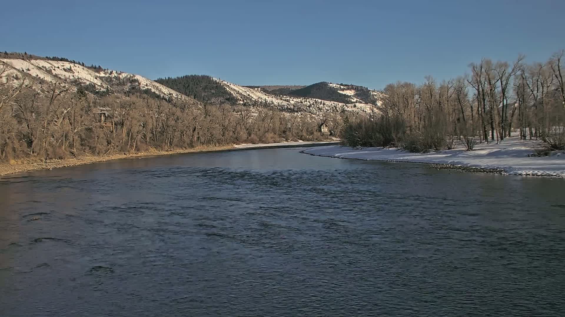 A gently flowing river meanders through a snow-dusted valley under a clear blue sky.