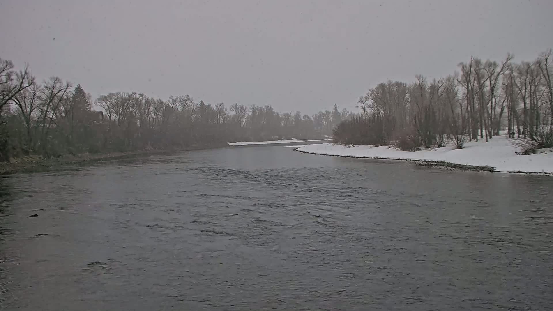 A gently curving river flows through a snow-covered landscape under a gray, overcast sky.