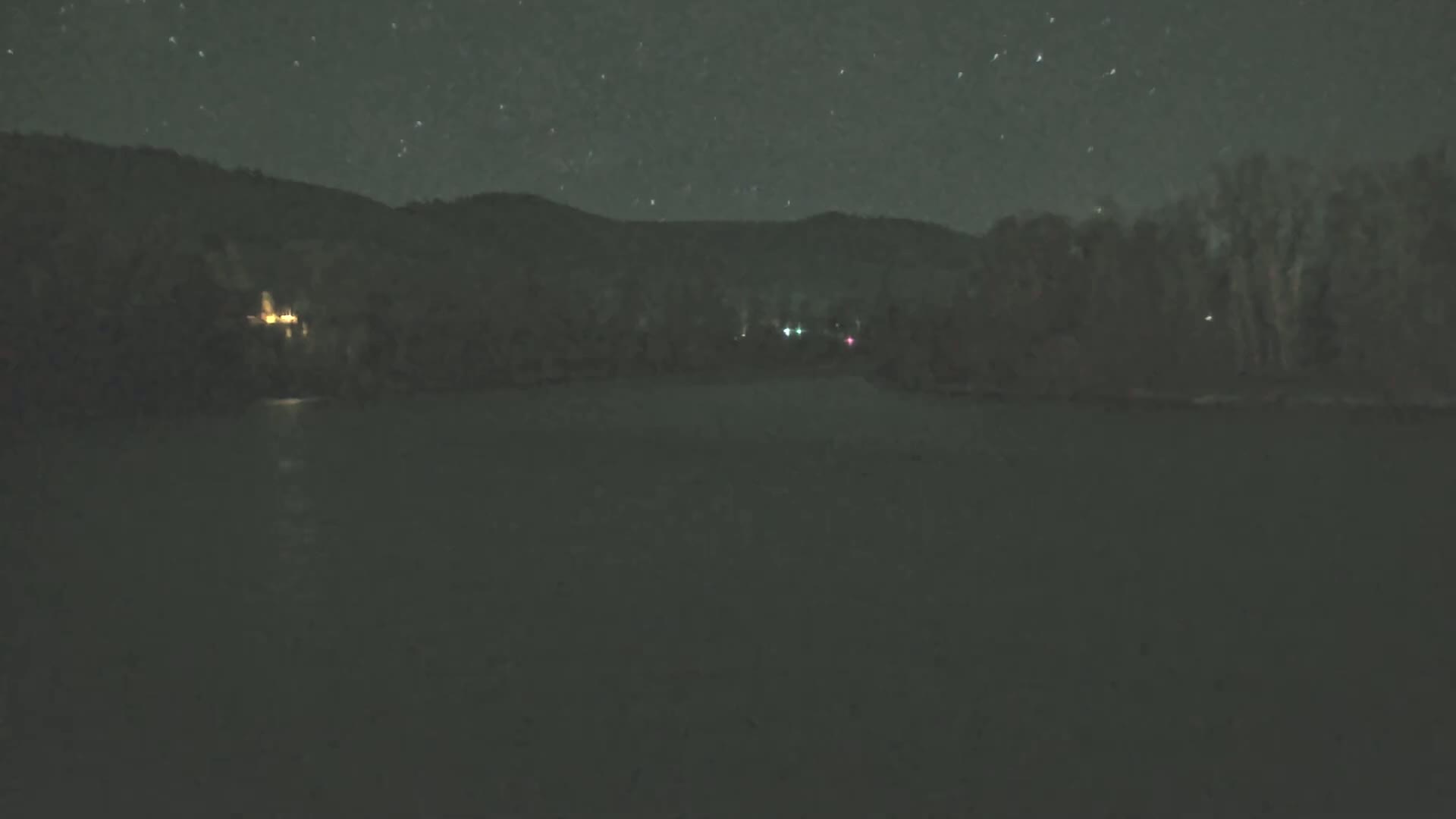 A dark body of water sits before a silhouetted shoreline under a starry night sky.