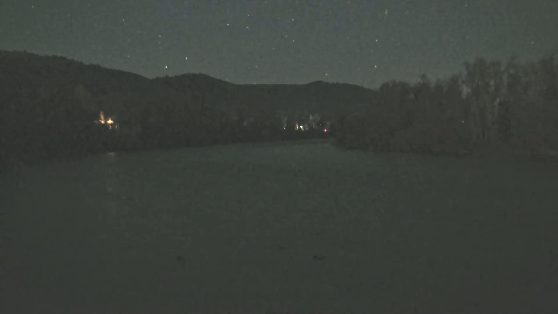 A dark body of water sits before a dimly lit shoreline under a starry night sky.