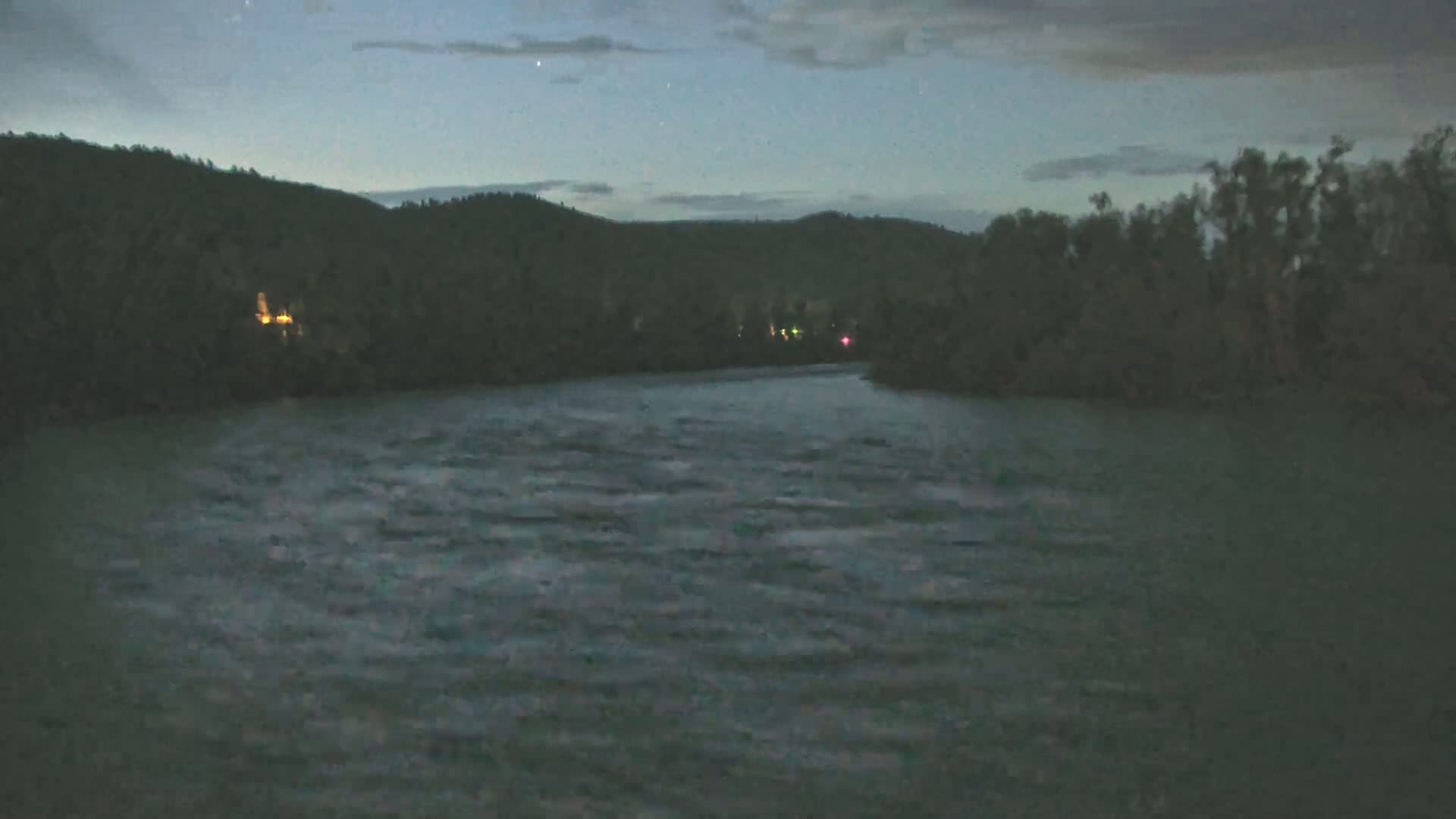 Under a dark, mostly clear night sky, a wide, dark river flows past tree-lined banks.