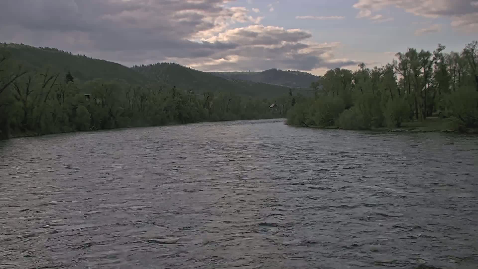 A wide, gently flowing river curves around a verdant shoreline under a partly cloudy sky.