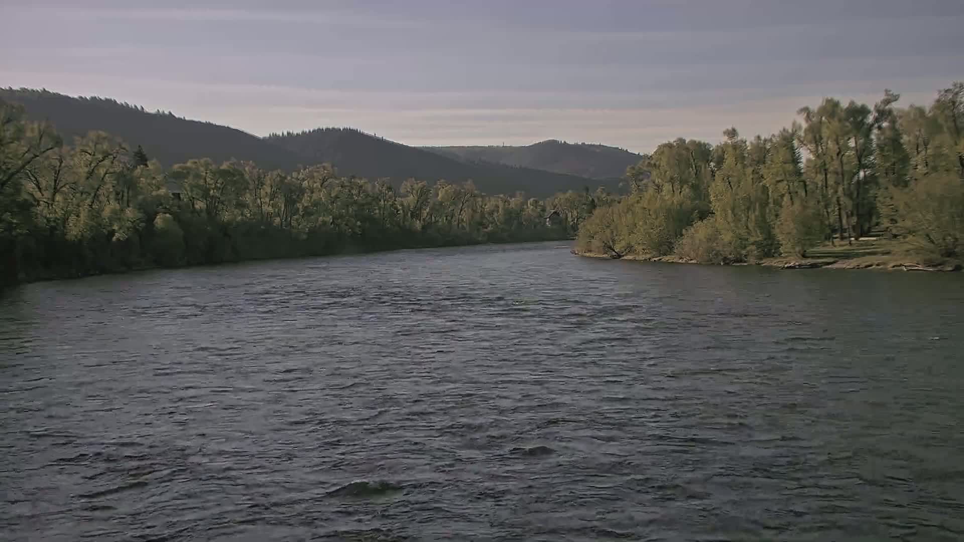 A gently flowing river winds through a verdant valley under a mostly clear sky.