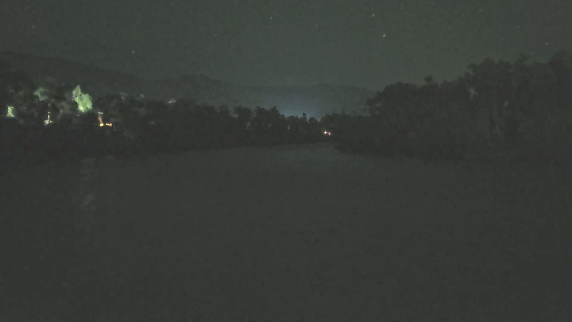 A dark, nighttime scene shows a line of trees and distant hills under a starry sky.