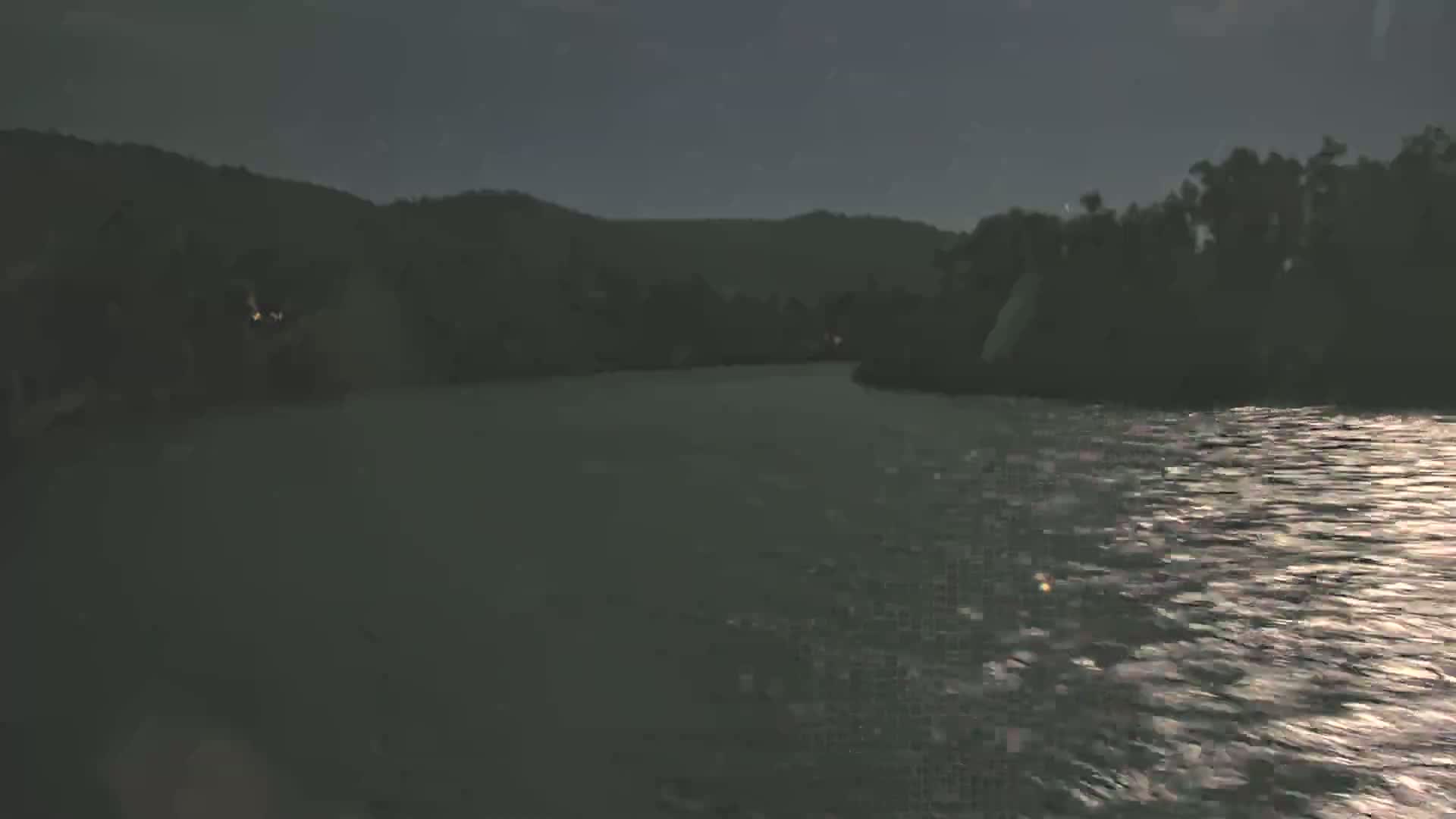 A dark body of water reflects the moonlight, with shadowy hills and trees lining its banks at night.