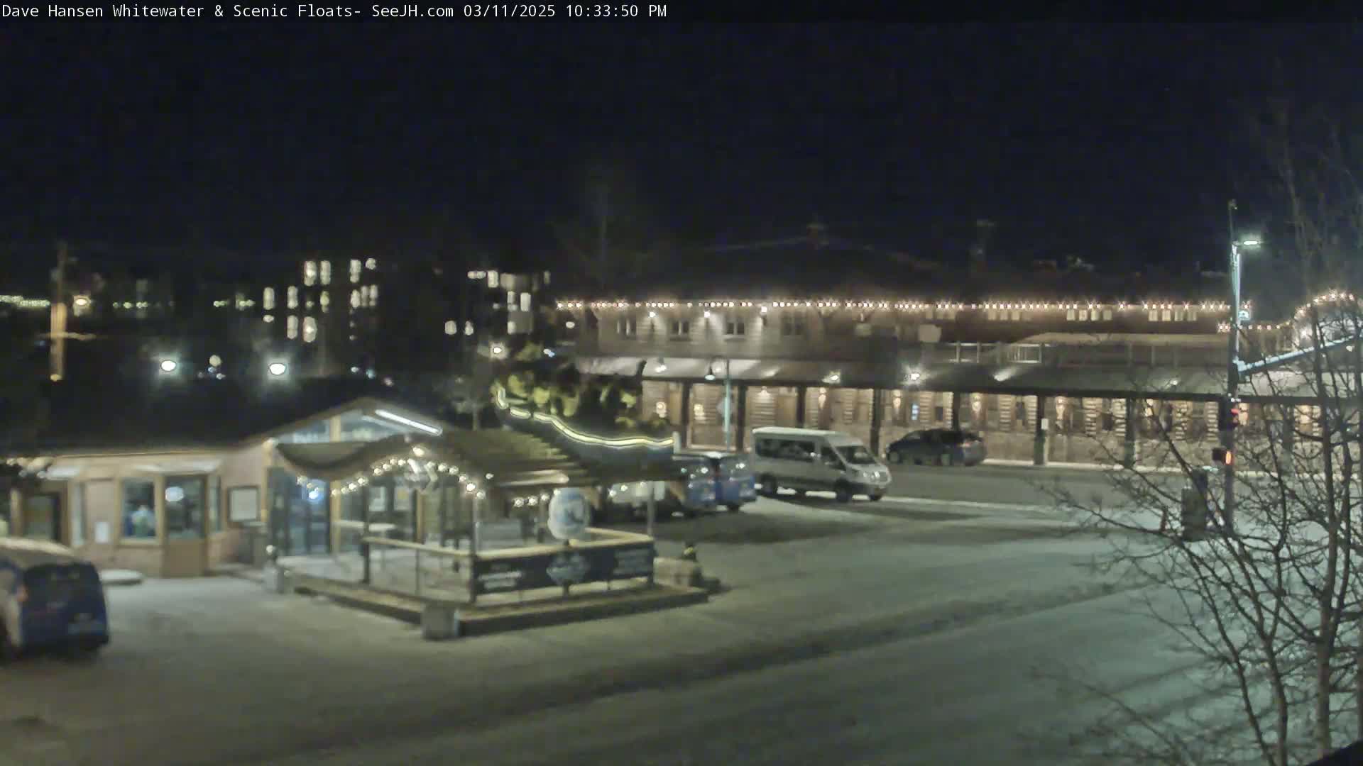 A nighttime view of a snow-covered parking lot and buildings, illuminated by artificial lights.
