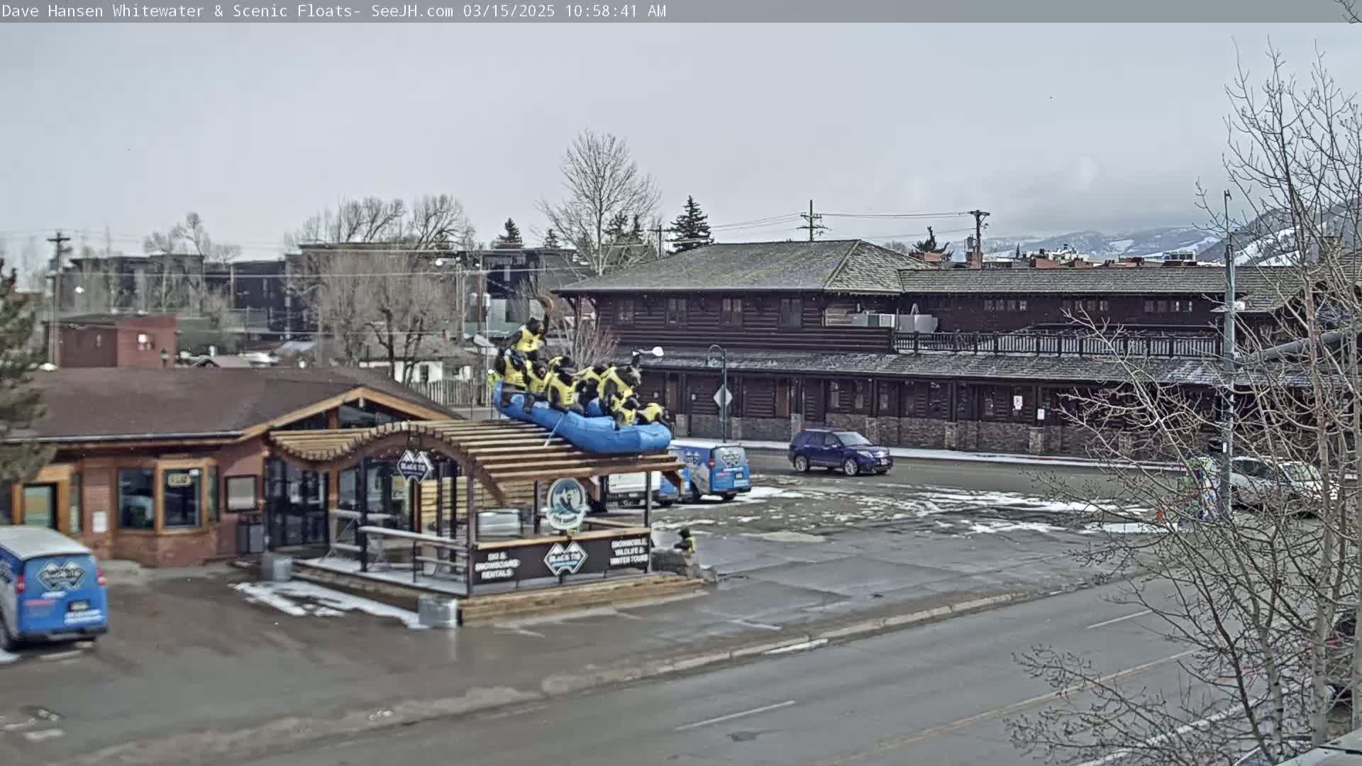 A blue raft with people in it sits on a building's roof in a parking lot, with overcast skies and patchy snow on the ground.