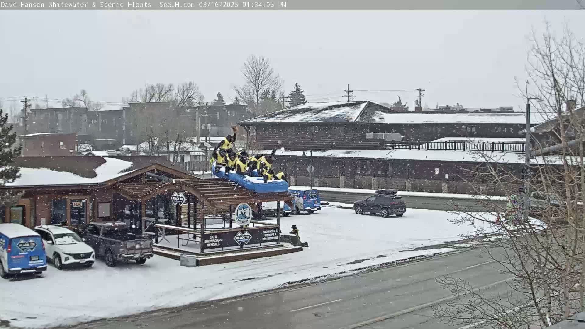 A group of people in yellow life vests are perched atop a raft on a snow-covered structure next to a road in a snowstorm.