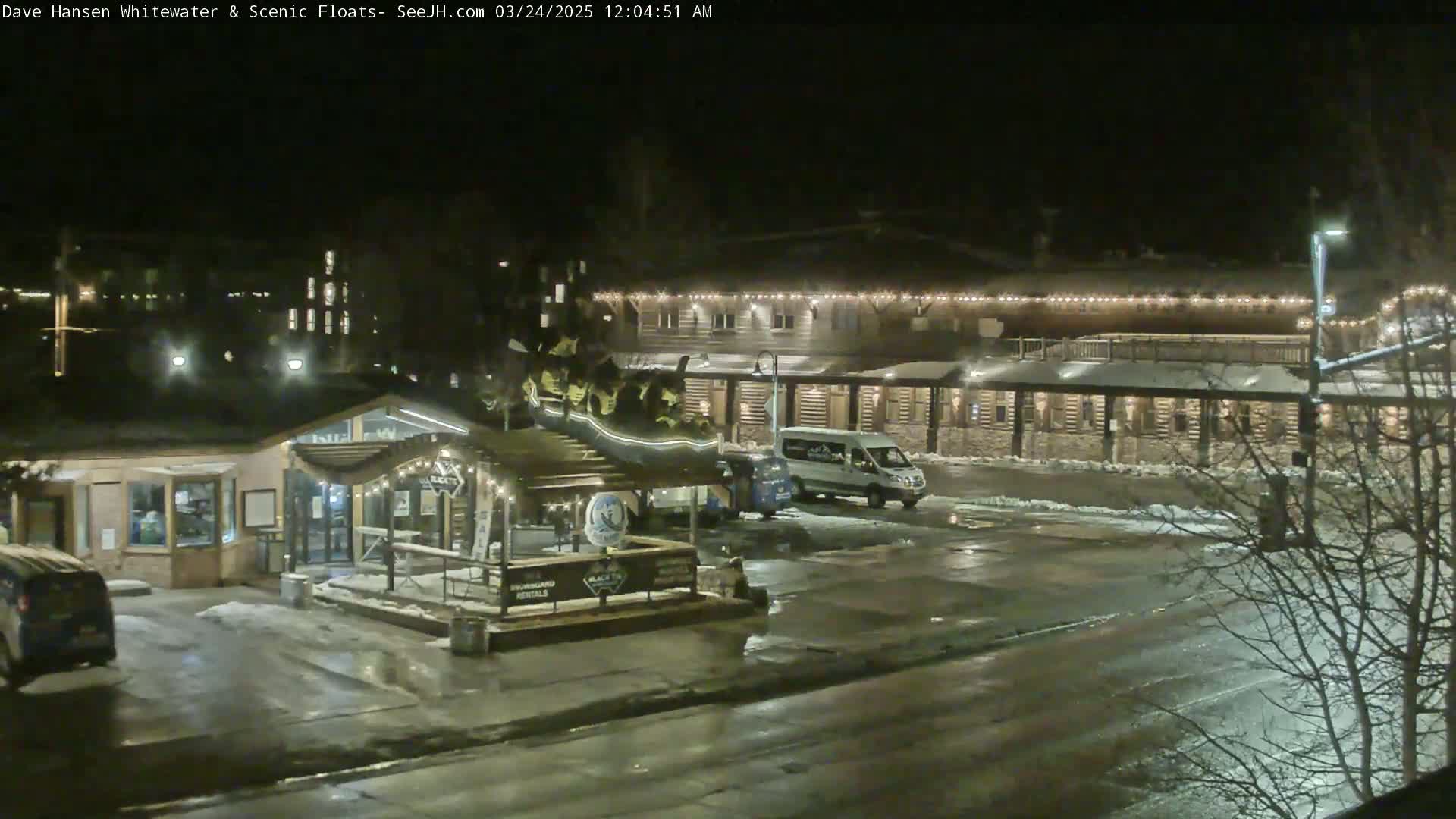 A nighttime view of a parking lot and building complex with some snow and ice on the ground, illuminated by streetlights and building lights.