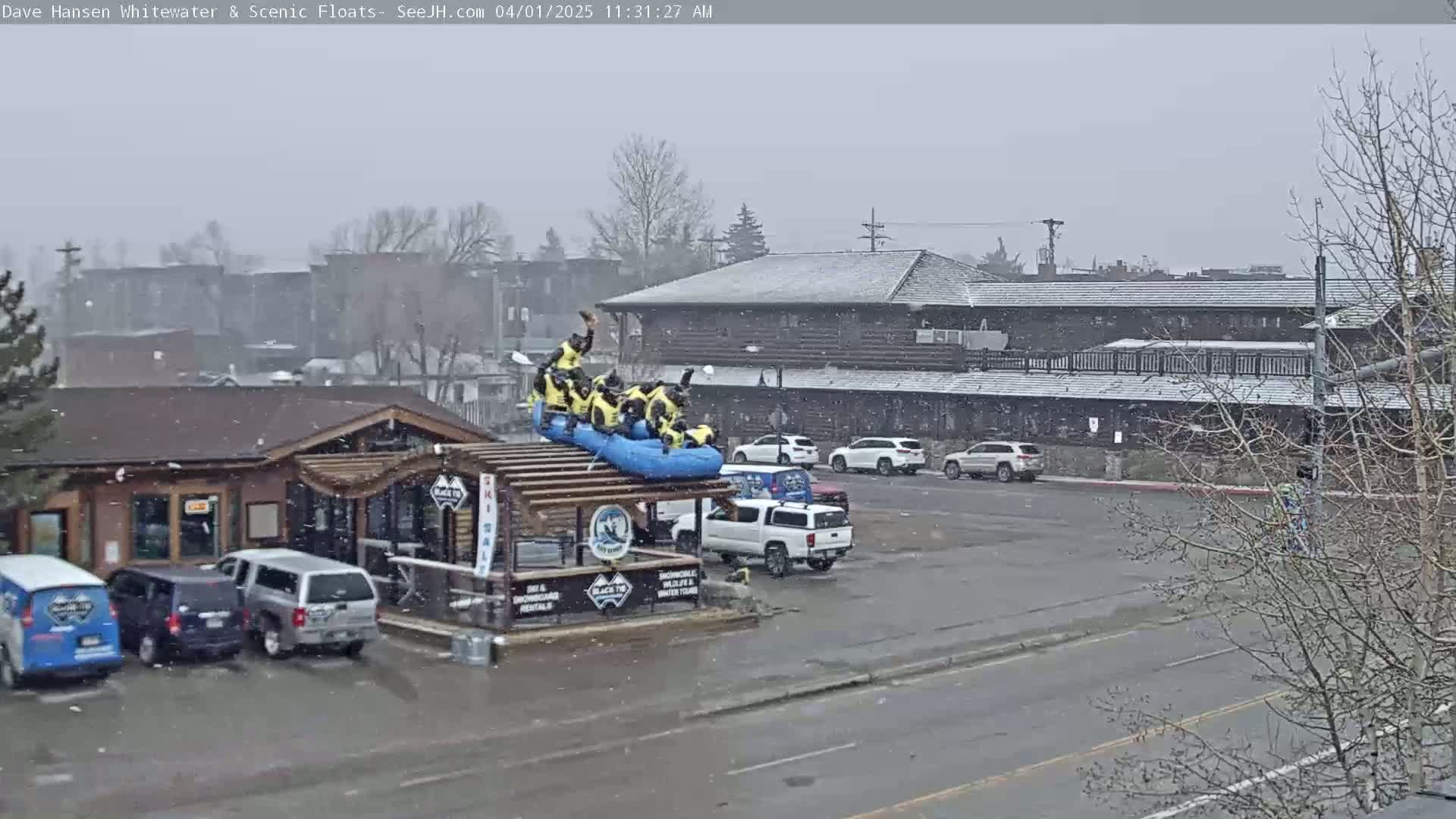 A group of people in a raft are on top of a building in a snowy parking lot.