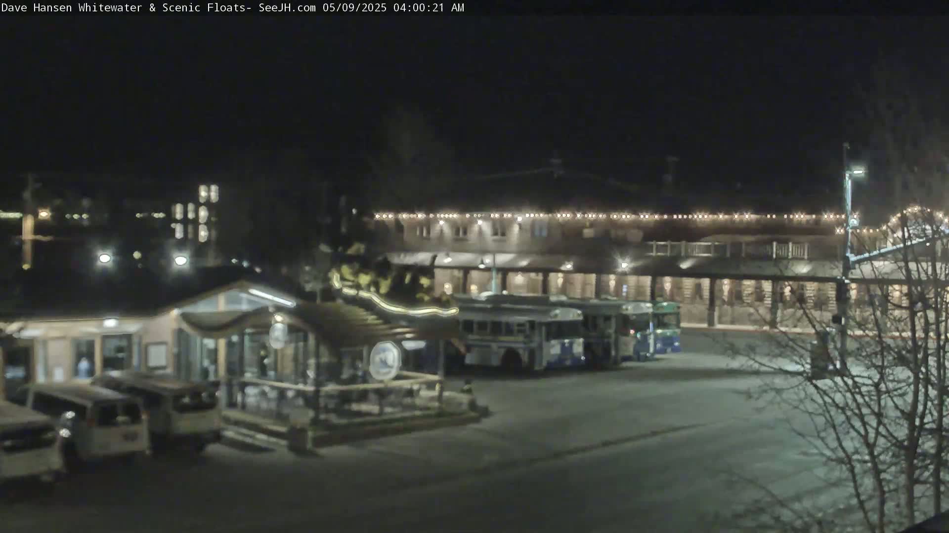At night, a parking lot with several vehicles, including buses, is adjacent to a building with exterior lighting.