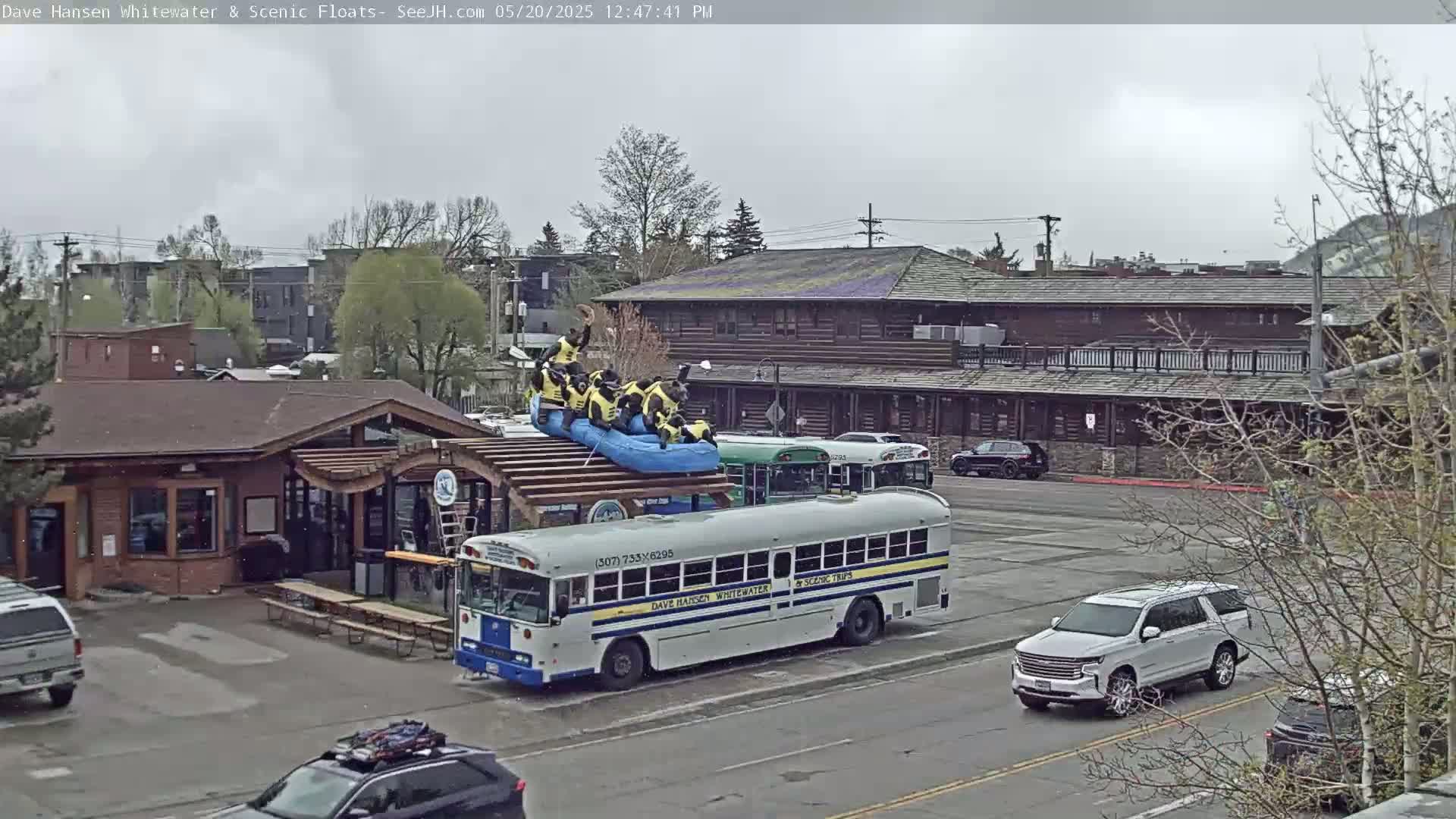 A group of people in yellow life vests are on a raft on top of a school bus in a parking lot on an overcast day.