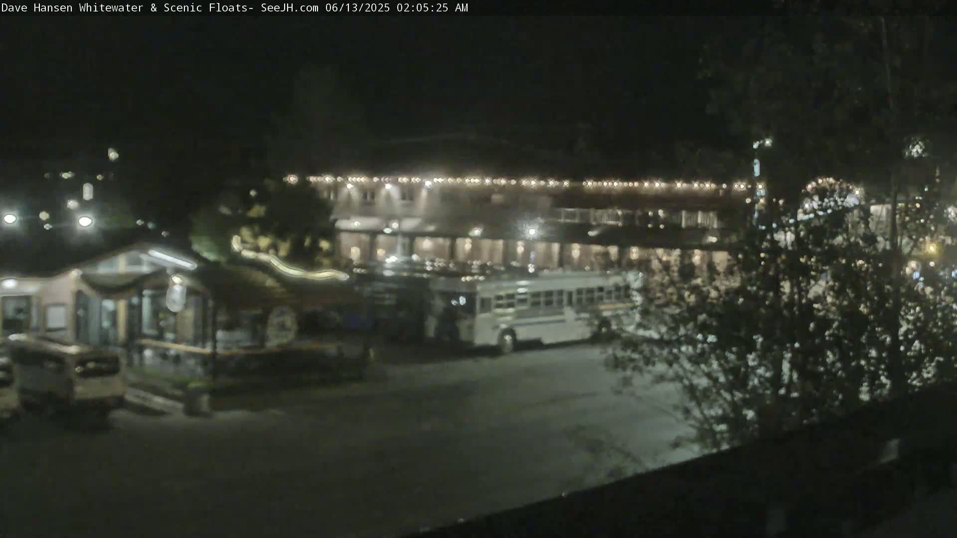 At night, a parking lot with a building and several vehicles, including a bus, is dimly lit.