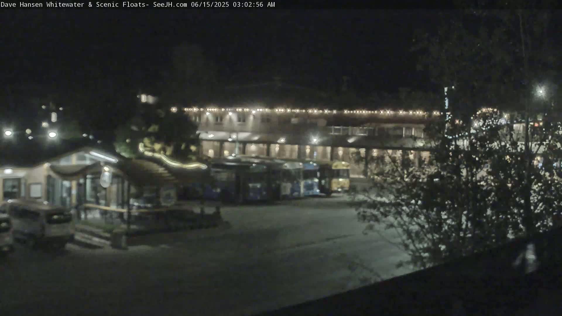 A nighttime view of a parking lot with several buses parked near a building illuminated with string lights.