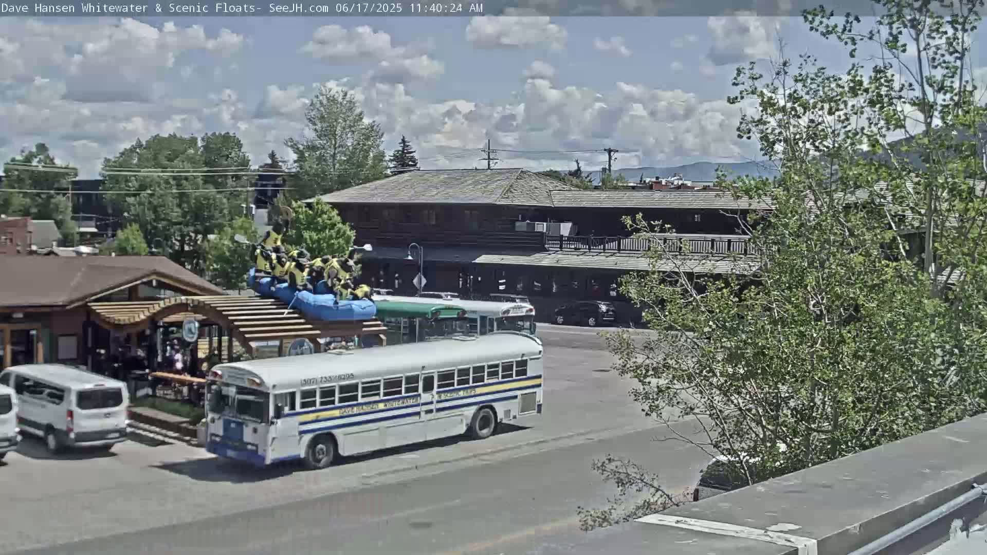 A partly cloudy day shows a street scene with a bus, several cars, and a building with a raft on its roof.