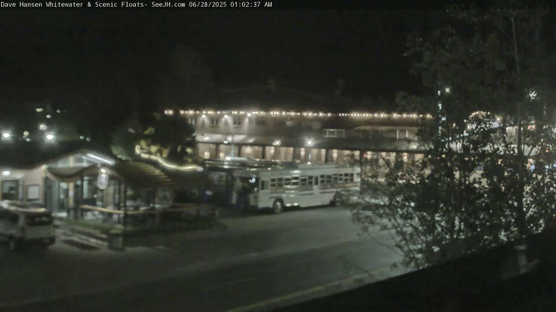 A nighttime view of a street scene with a bus parked in front of a building, surrounded by trees and other structures under clear, dark skies.