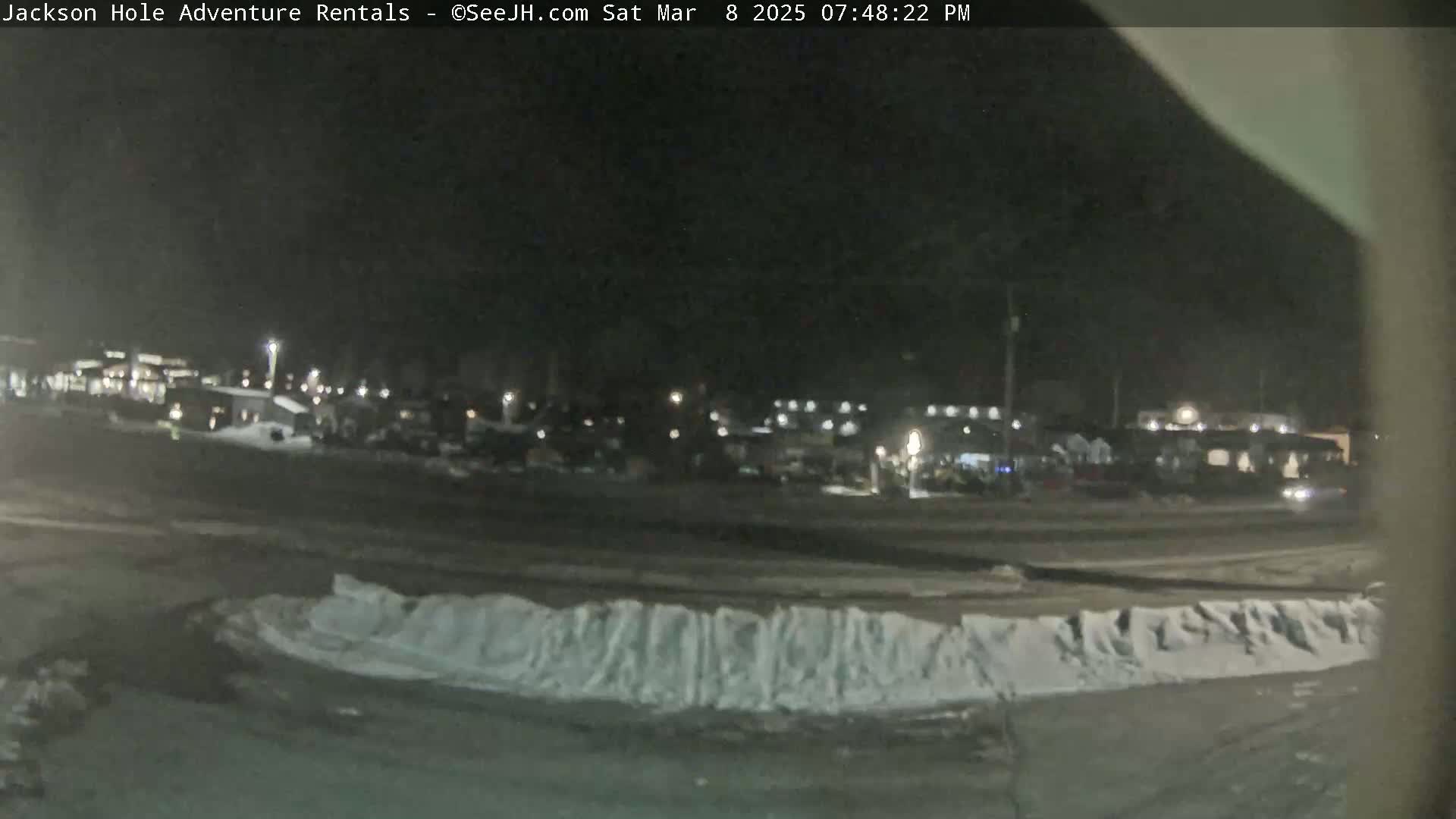A nighttime view of a snow-covered parking lot and a line of buildings under a dark sky.
