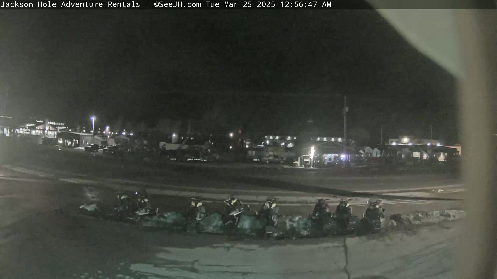 At night, several snowmobiles are parked in a row near a dimly lit building complex under a dark sky.