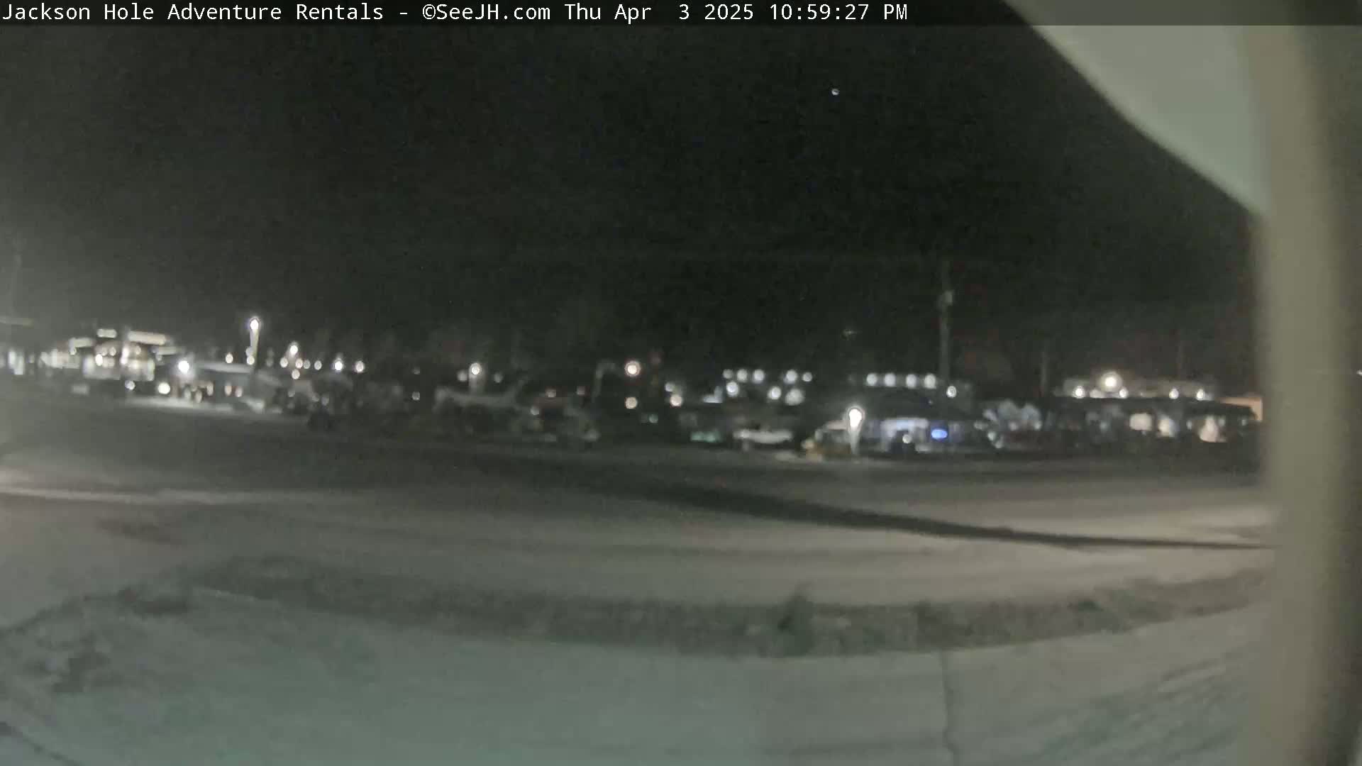 A nighttime, snow-covered parking lot with many vehicles parked, is visible under a dark sky.