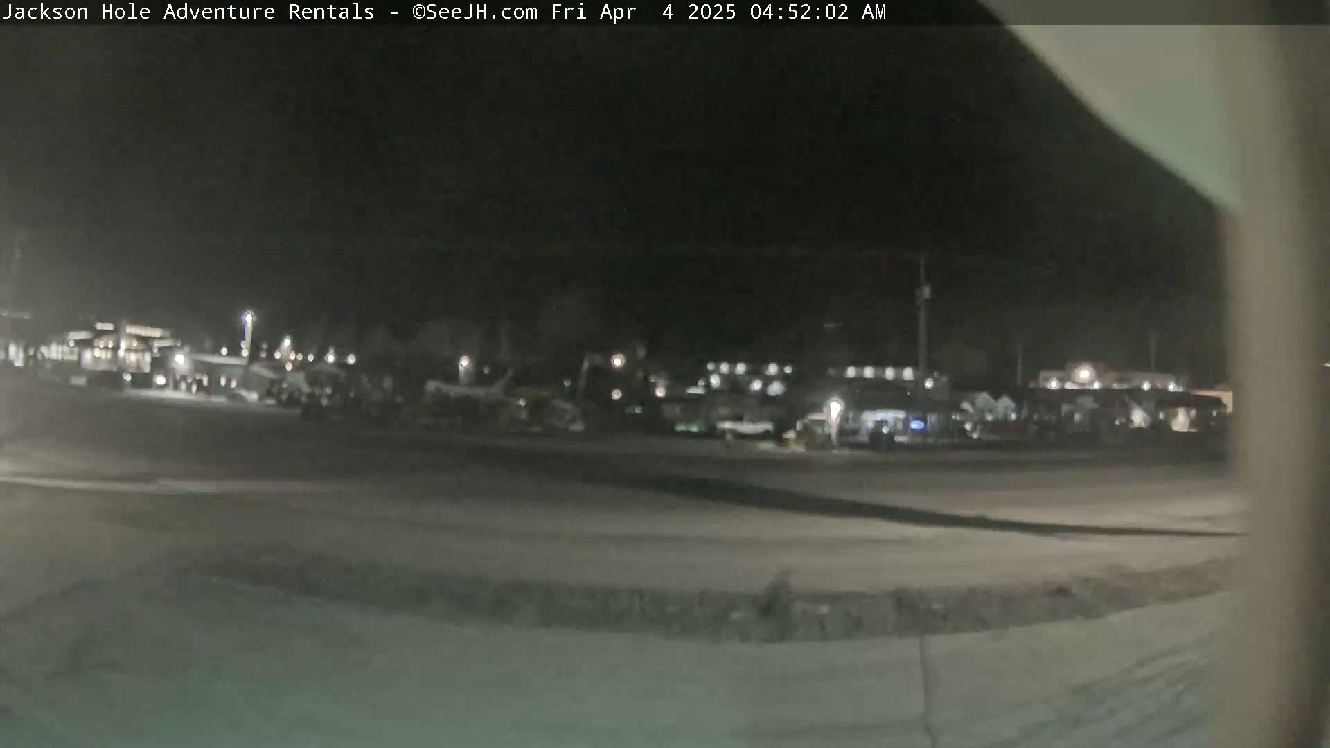 A nighttime, low-light view of a parking lot filled with numerous vehicles, some appearing to be construction or utility equipment.