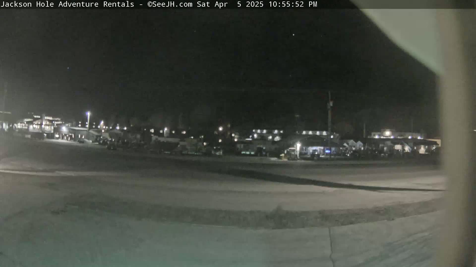 A nighttime, outdoor view of a parking lot with numerous vehicles and buildings in the distance under a clear, dark sky.