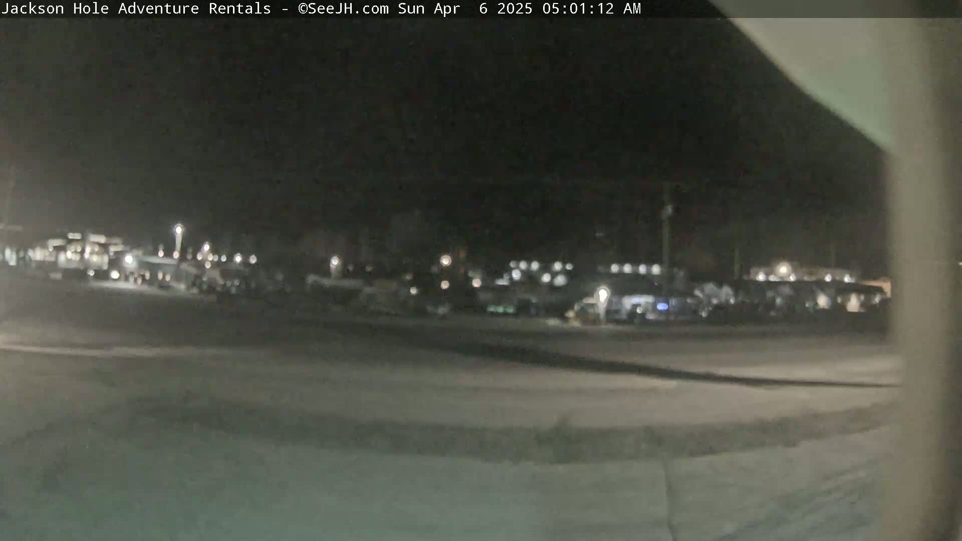A nighttime, blurry view of a parking lot with many vehicles parked, under a dark sky.