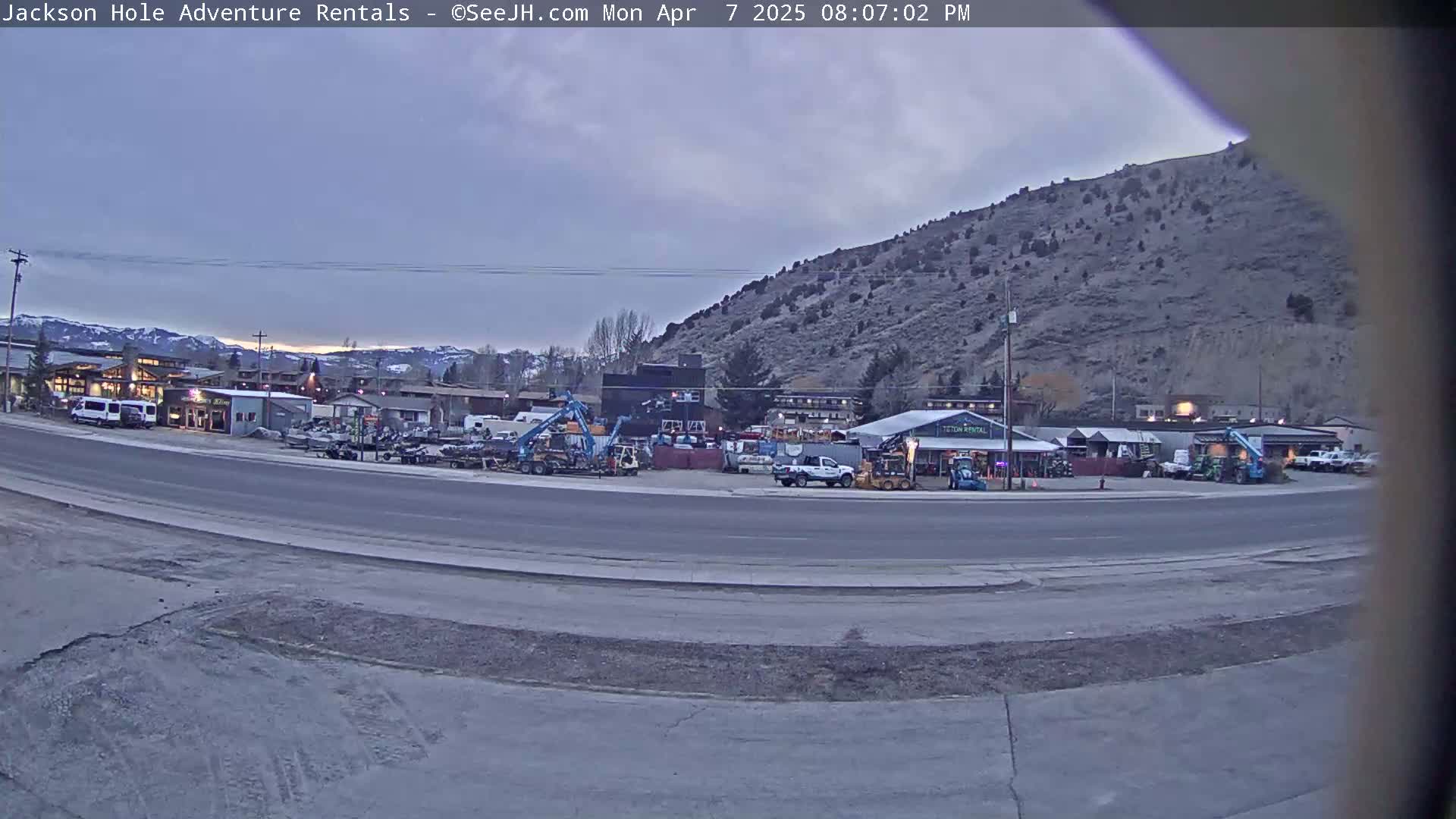 A parking lot filled with various vehicles and equipment sits before a hill under an overcast sky.
