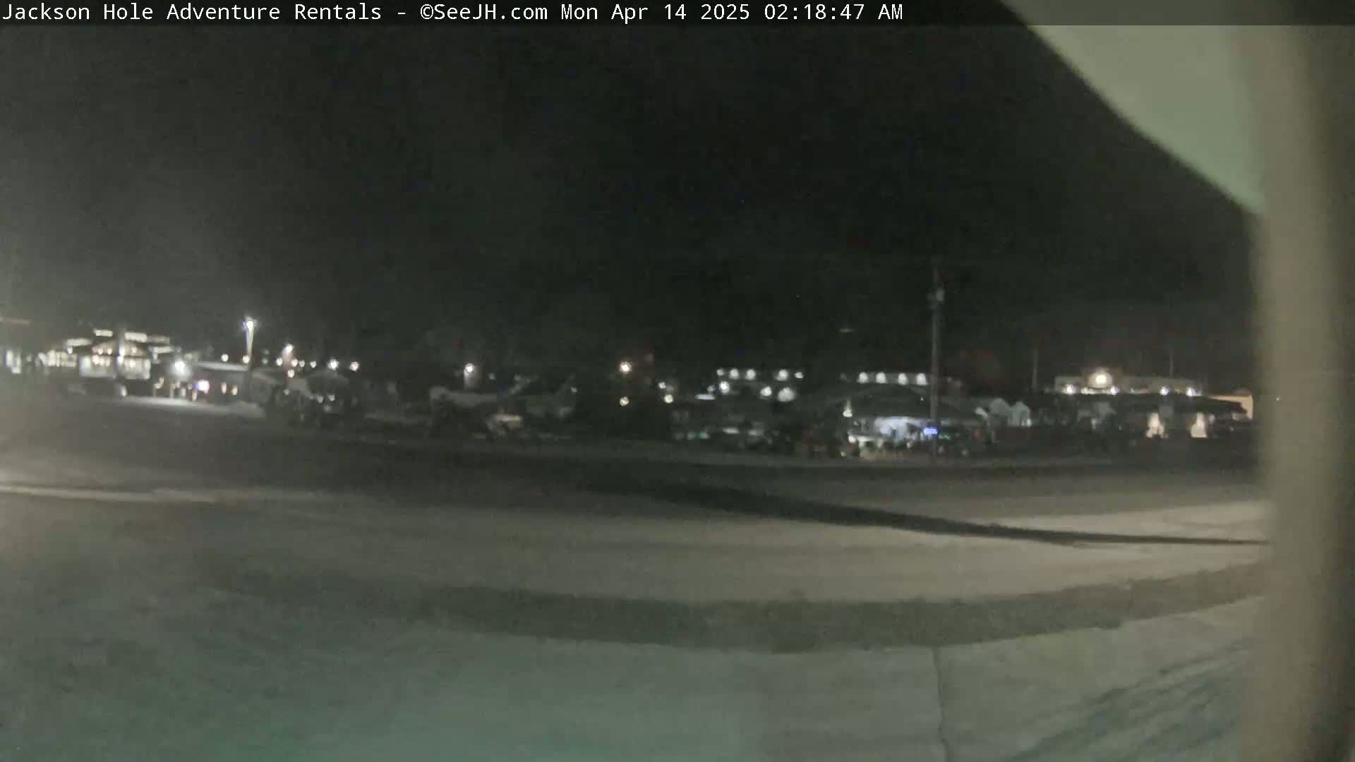 A nighttime, low-light view of a parking lot with several vehicles and buildings in the background.