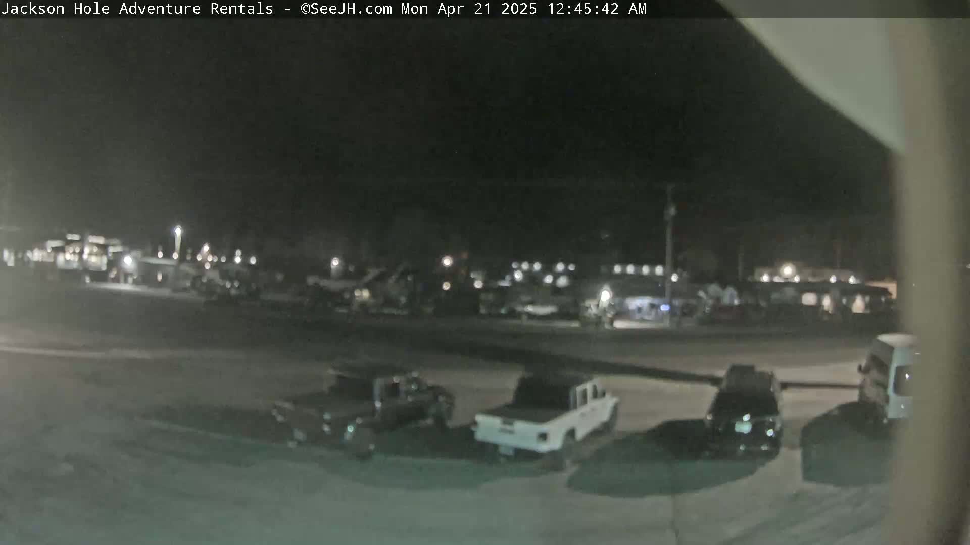 A nighttime, outdoor parking lot with several trucks and SUVs parked, and a few other vehicles in the background.