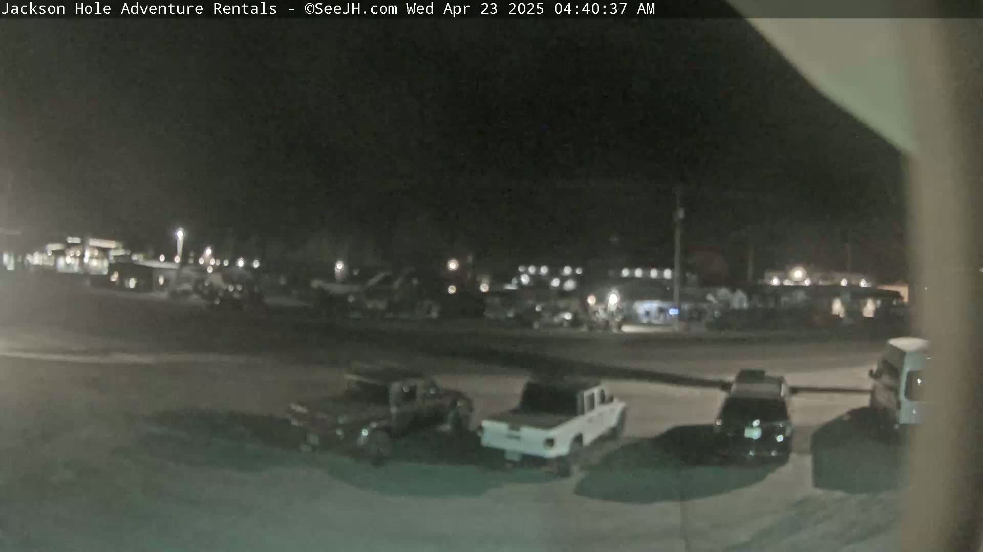 A nighttime, outdoor view shows several vehicles parked in a lot, with a few more vehicles visible in the distance.