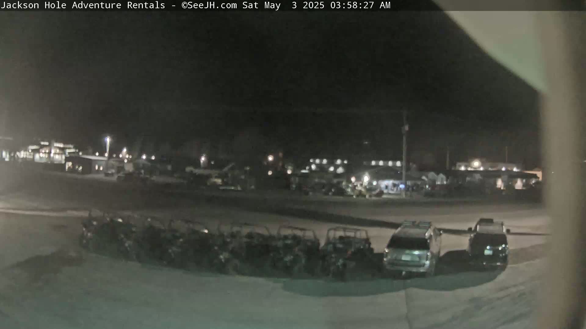 A nighttime, outdoor scene shows a parking lot with several all-terrain vehicles and cars parked, under dark, clear skies.
