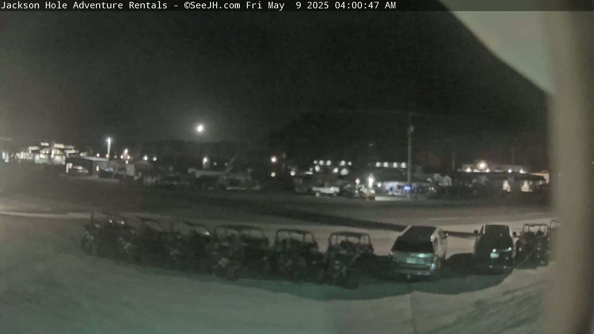 A nighttime, moonlit scene shows a parking lot with numerous small, four-wheeled vehicles parked in a row, along with several other cars and SUVs.
