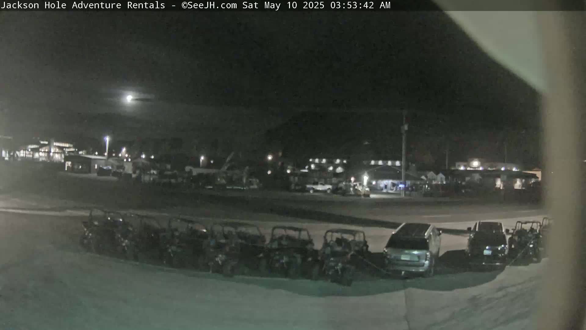 A nighttime view shows a row of parked all-terrain vehicles in front of a building complex under a clear, moonlit sky.