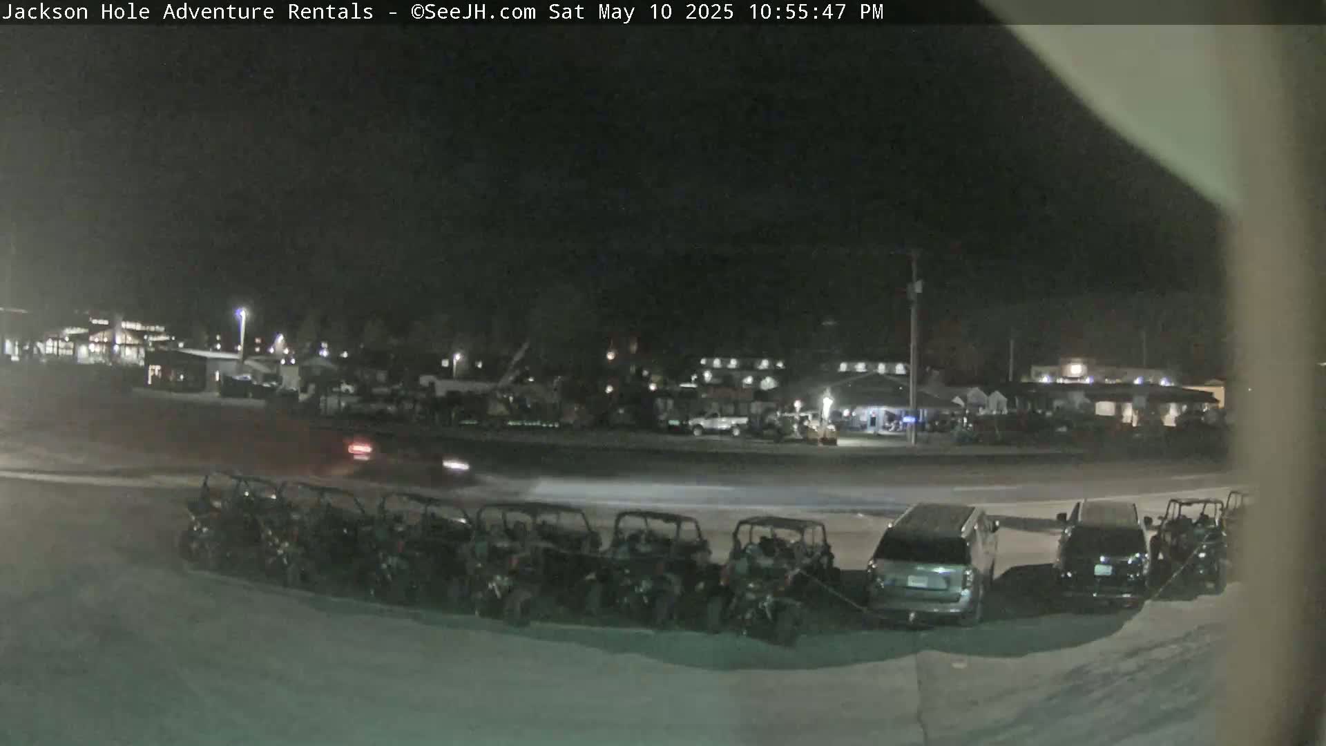 At night, a row of parked all-terrain vehicles sits in front of a parking lot and buildings under a dark sky.