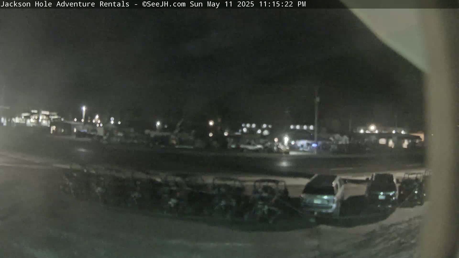 A nighttime view of a parking lot filled with vehicles, some of which appear to be utility terrain vehicles, under dark, possibly snowy conditions.