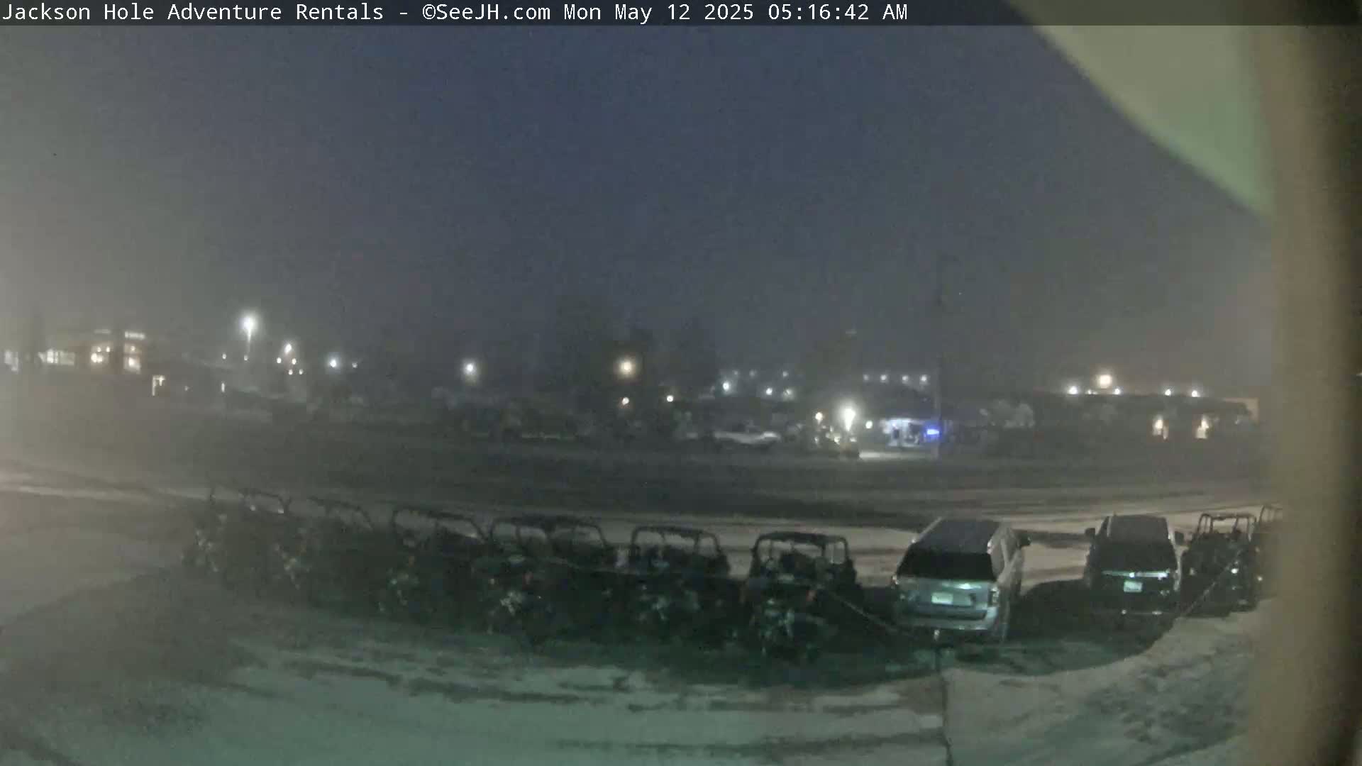 A row of parked off-road vehicles sits in a dimly lit parking lot shrouded in fog or light snow at night.