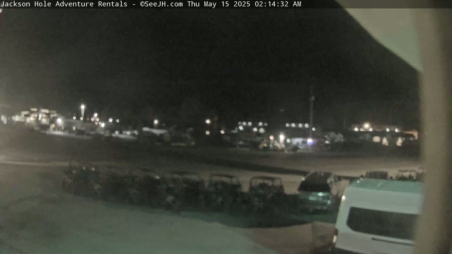 A nighttime, outdoor scene shows numerous vehicles parked in a lot, including several small, off-road type vehicles, cars, and a van.