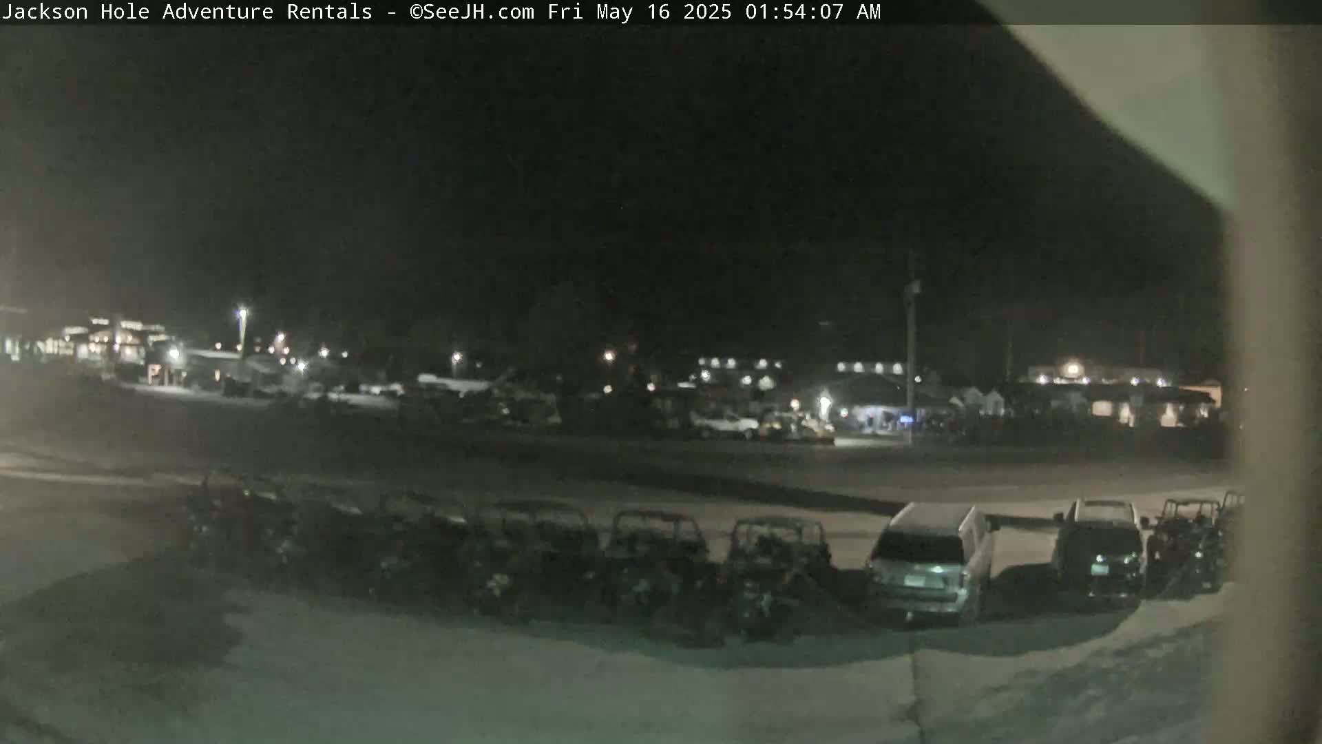 A nighttime, outdoor scene shows a row of parked ATVs and a few cars in a parking lot in front of a building under dim lighting.