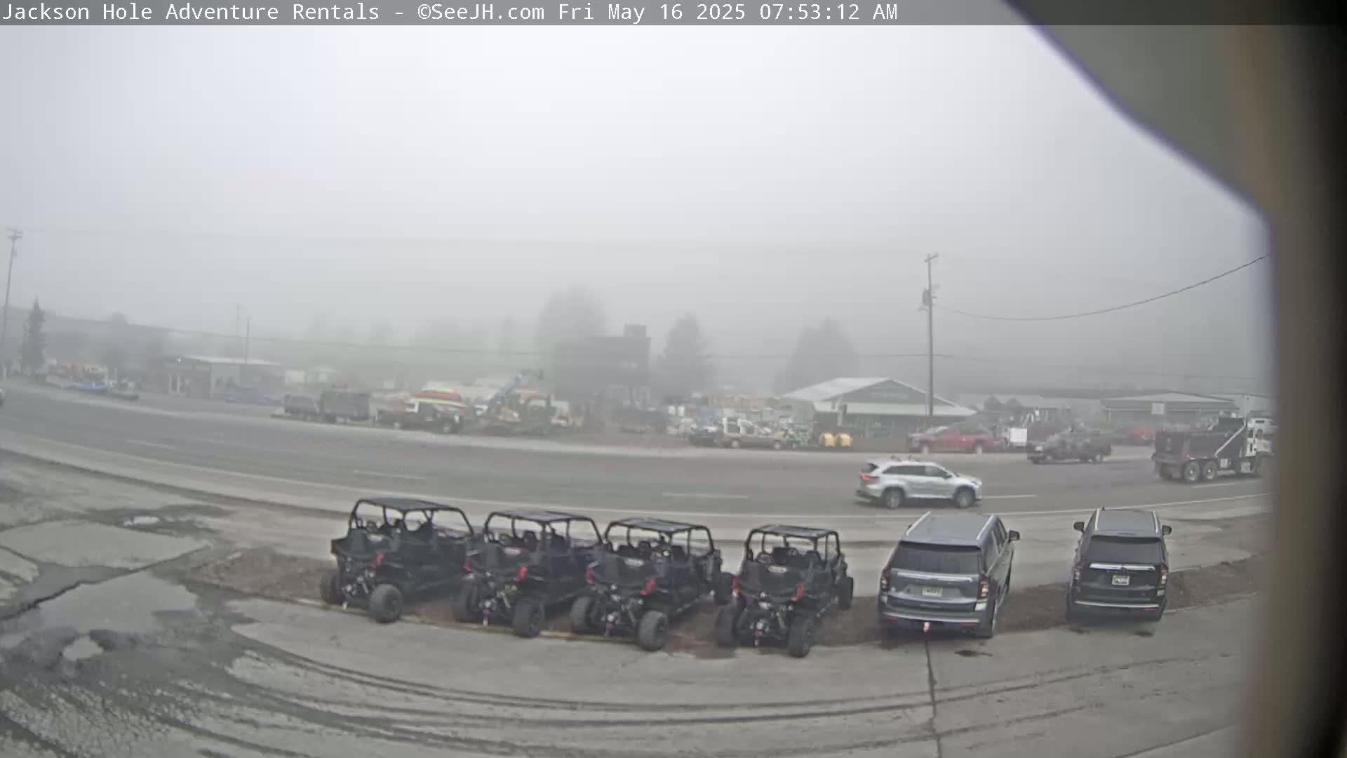 Several all-terrain vehicles are parked in a row next to a road in a foggy area, with cars and other vehicles visible in the background.