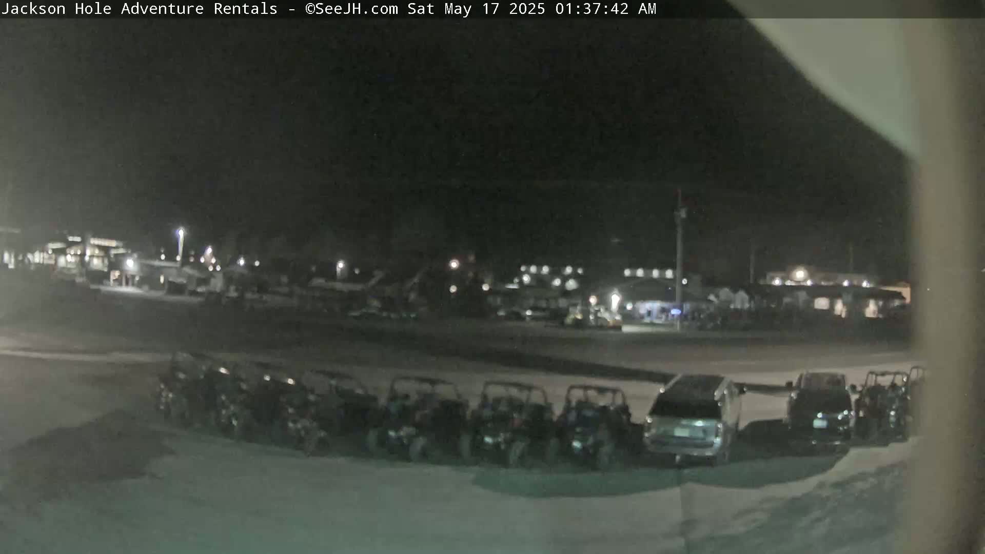 A nighttime view of a parking lot with several off-road vehicles and cars parked near a building under dark, clear skies.