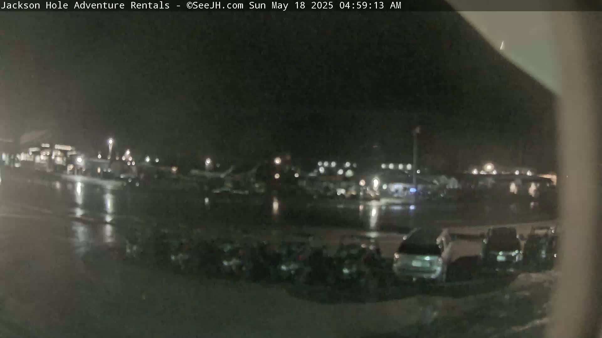A nighttime, wet parking lot with many vehicles is visible, along with some distant lights and buildings.