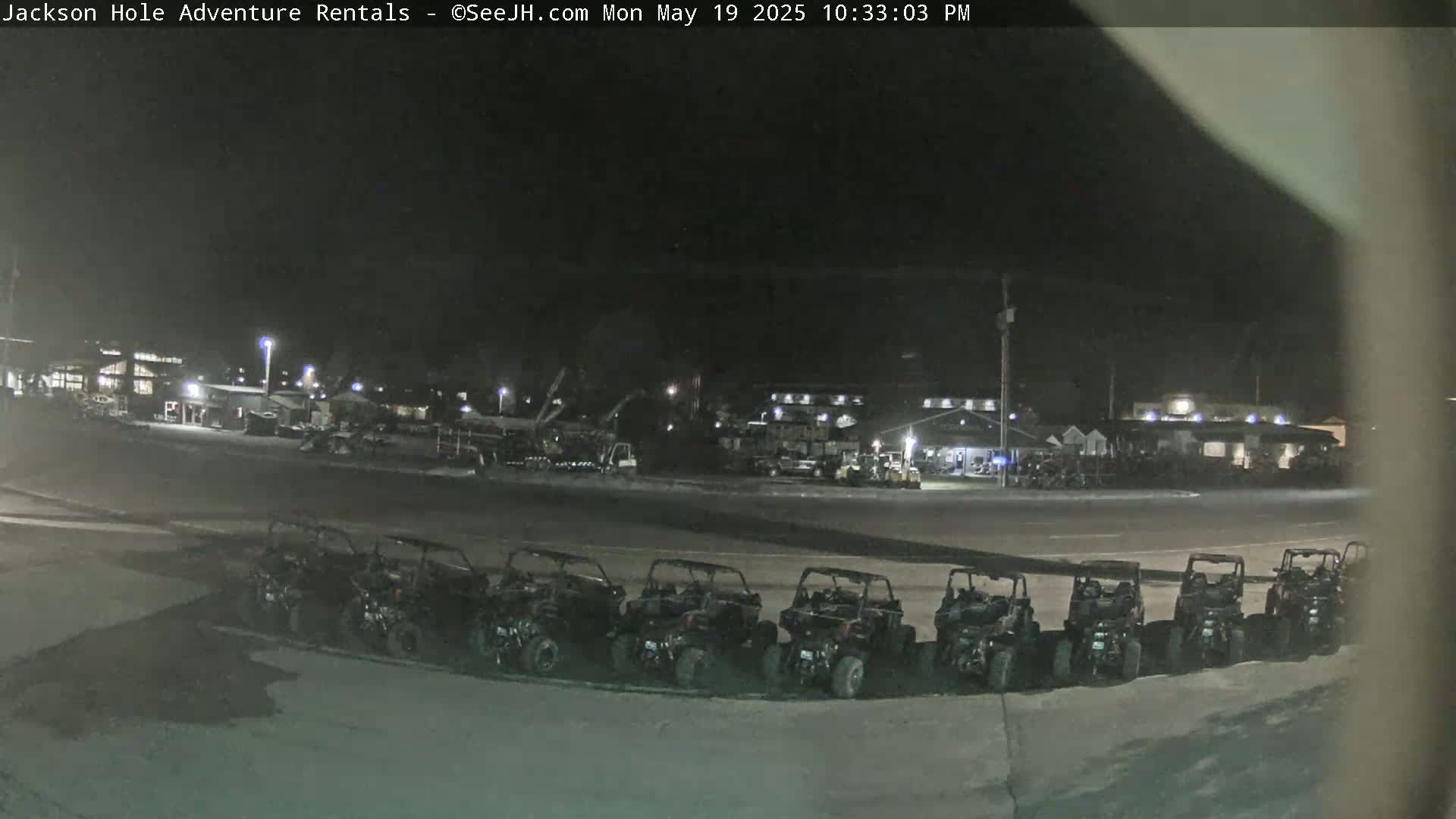 A row of parked ATVs sits in a parking lot at night, in front of a building complex under a dark sky.